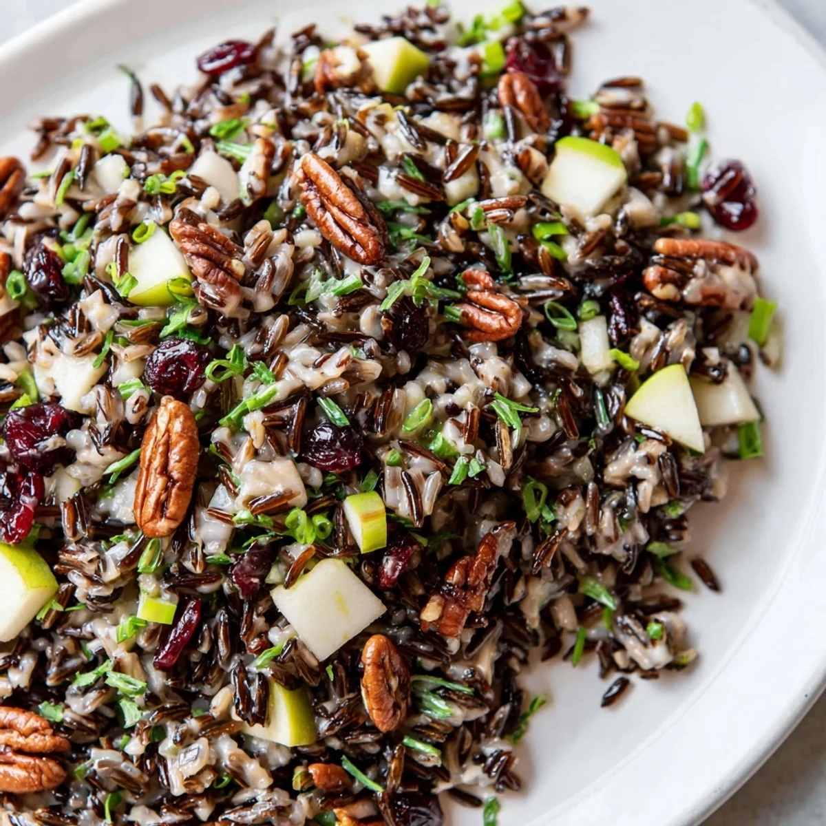 A close-up view of Wild Rice Harvest Salad in a white bowl, featuring toasted pecans, dried cranberries, and fresh herbs tossed in a light vinaigrette.  
