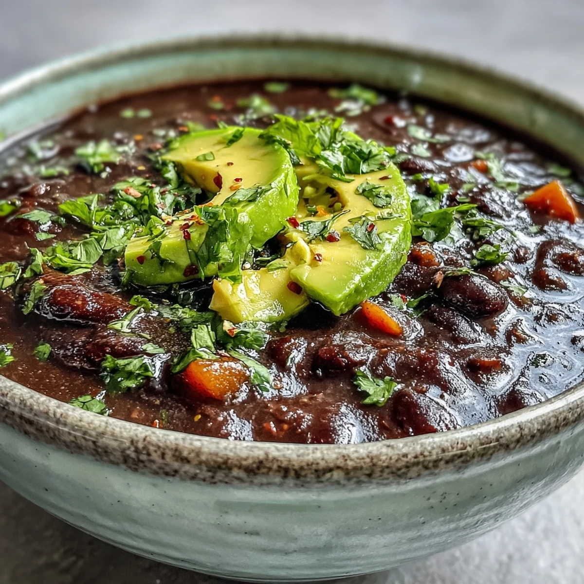 Close-up of a creamy Black Bean Soup in a white bowl, topped with sour cream and red onions, with a spoon ready to eat.