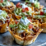 Golden mini taco cups filled with seasoned meat, topped with fresh garnishes.