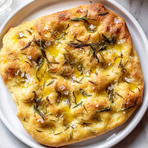 A close-up shot of a fluffy Simple Homemade Focaccia, drizzled with olive oil and herbs.