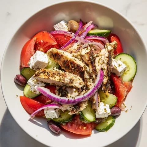 Freshly grilled chicken atop a vibrant Greek salad with olives, ready to enjoy.