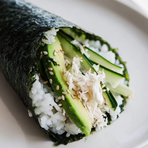 Freshly rolled sushi rice hand rolls showcasing layers of avocado, cucumber, and shredded crab wrapped in dark nori for a bite-sized treat.