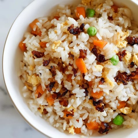 Steaming Black Garlic Fried Rice in a skillet, featuring sweet black garlic, mixed vegetables, and a drizzle of toasted sesame oil.  