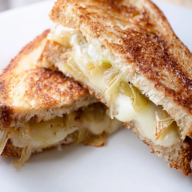 Golden, buttery Havarti & Caramelized Leek Grilled Cheese sandwich, sliced diagonally to reveal sweet leeks and creamy, melted cheese.