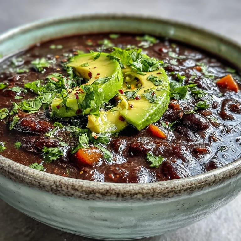 Close-up of a creamy Black Bean Soup in a white bowl, topped with sour cream and red onions, with a spoon ready to eat.