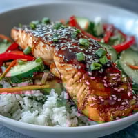 Flaky soy-ginger glazed salmon sits on fluffy jasmine rice, surrounded by vibrant julienned carrots and cucumbers.